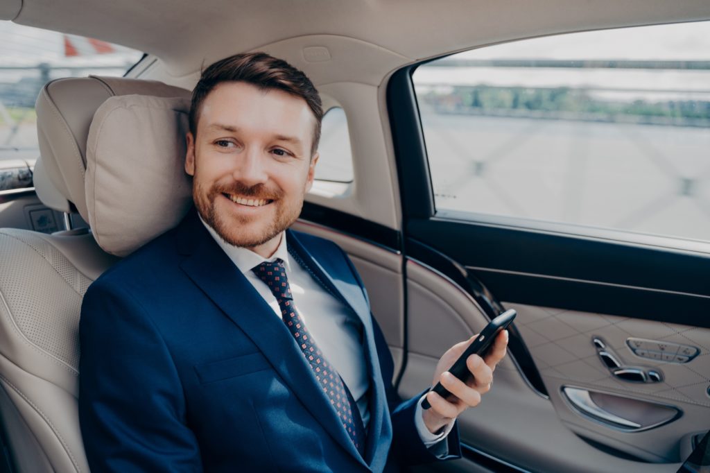 Corporate executive in elegant expensive tuxedo rides in luxury car