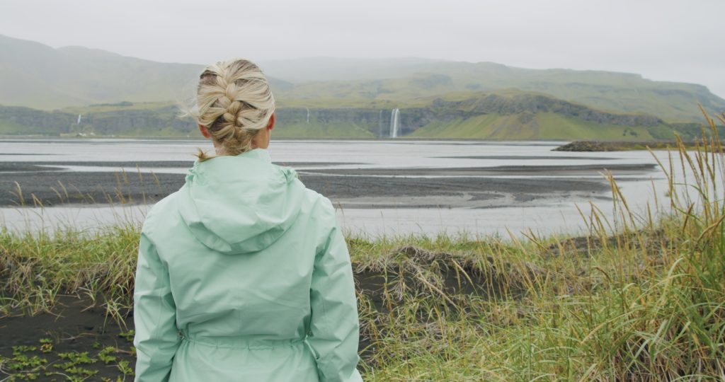 Woman enjoying Iceland Seljalandsfoss waterfall from far distance